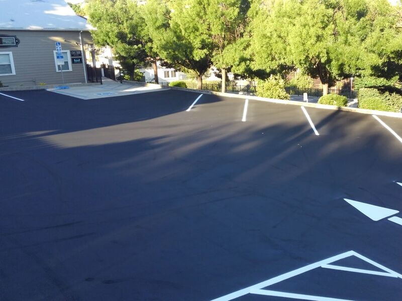Freshly sealcoated commercial parking lot with crisp white line striping and directional arrows by Asphalt Sealcoat Service